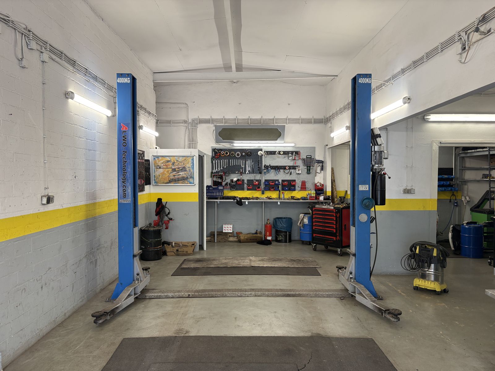 Leere Werkstatthalle mit blauer 2-Säulen-Hebebühne, Werkbank und Werkzeugwagen