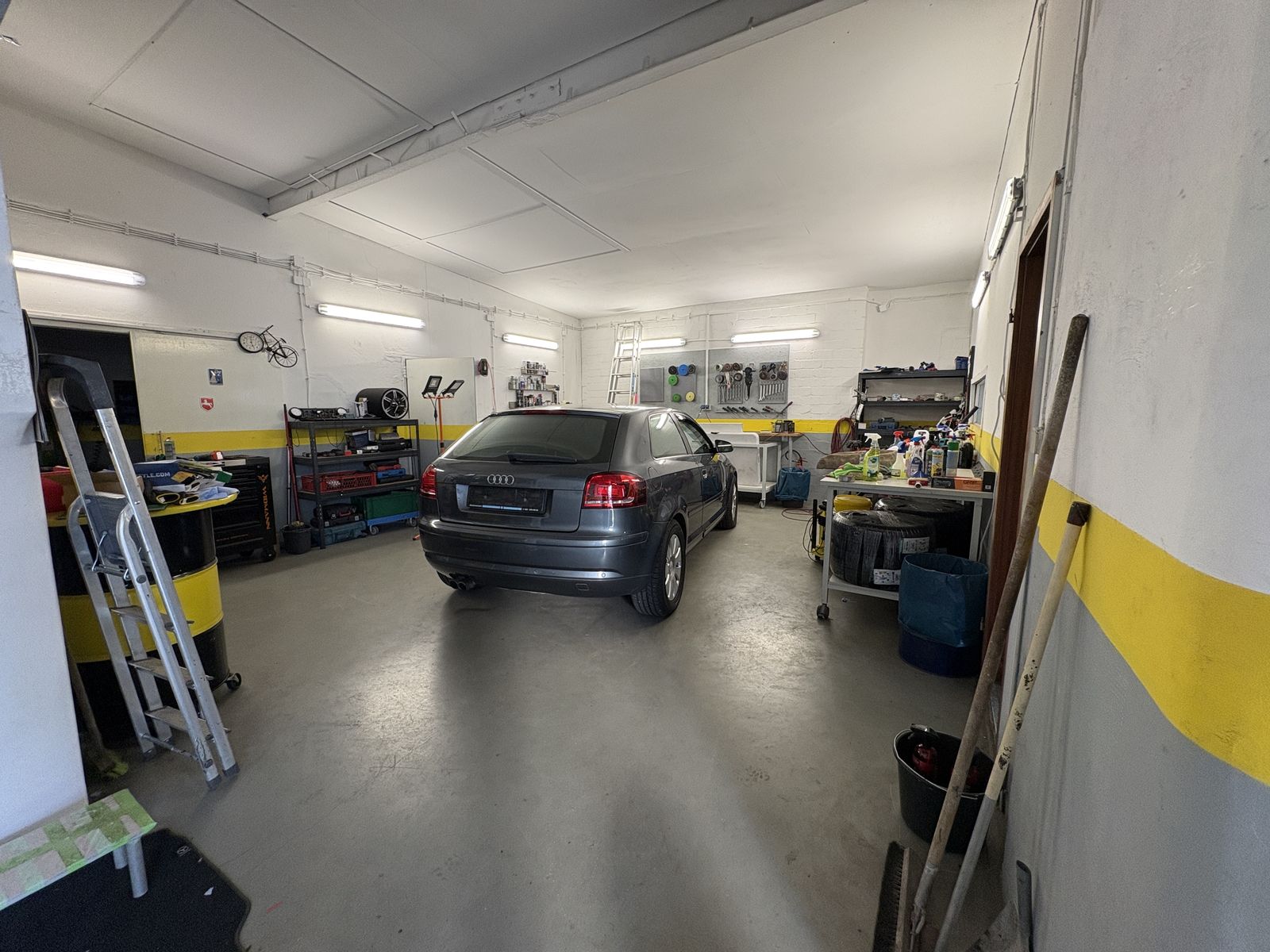 Zweite Werkstatthalle mit einem Audi, Regalen und Arbeitstisch